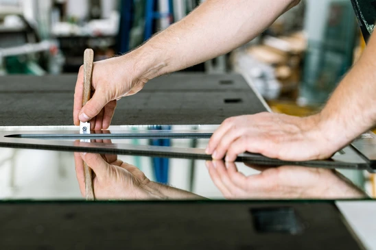Atelier de menuiserie avec artisan manipulant une règle graduée sur panneau de verre réfléchissant